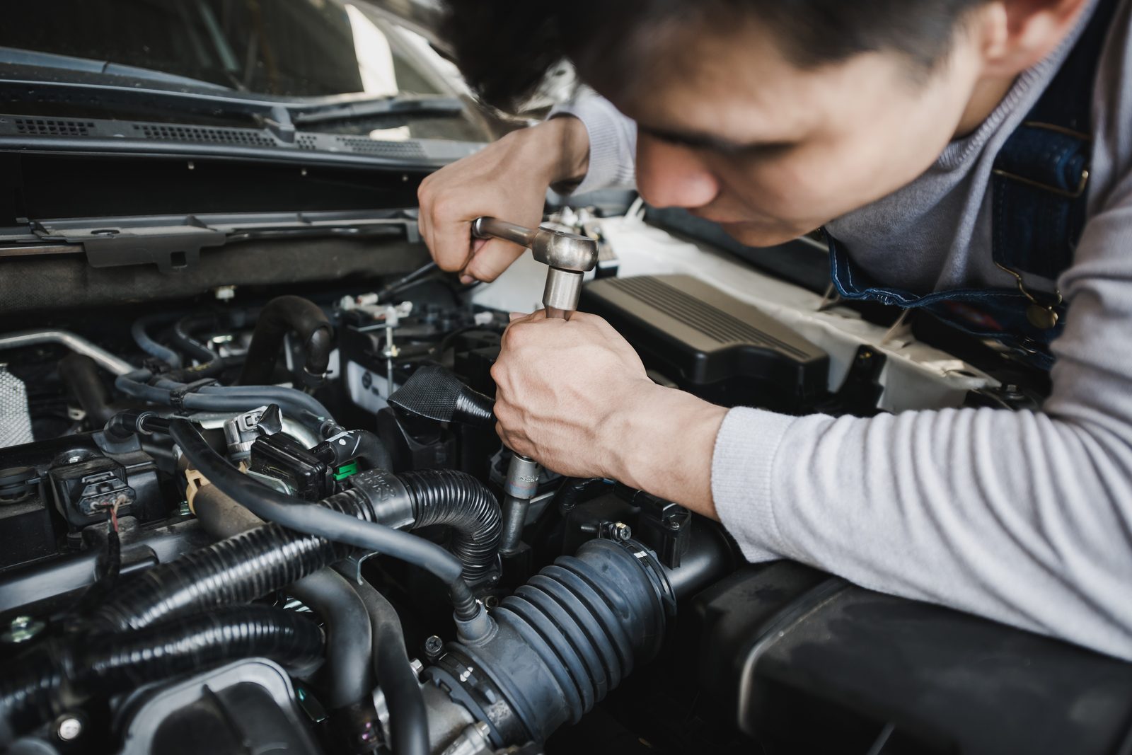 Automotive technician working under the hood of a car in a shop bay