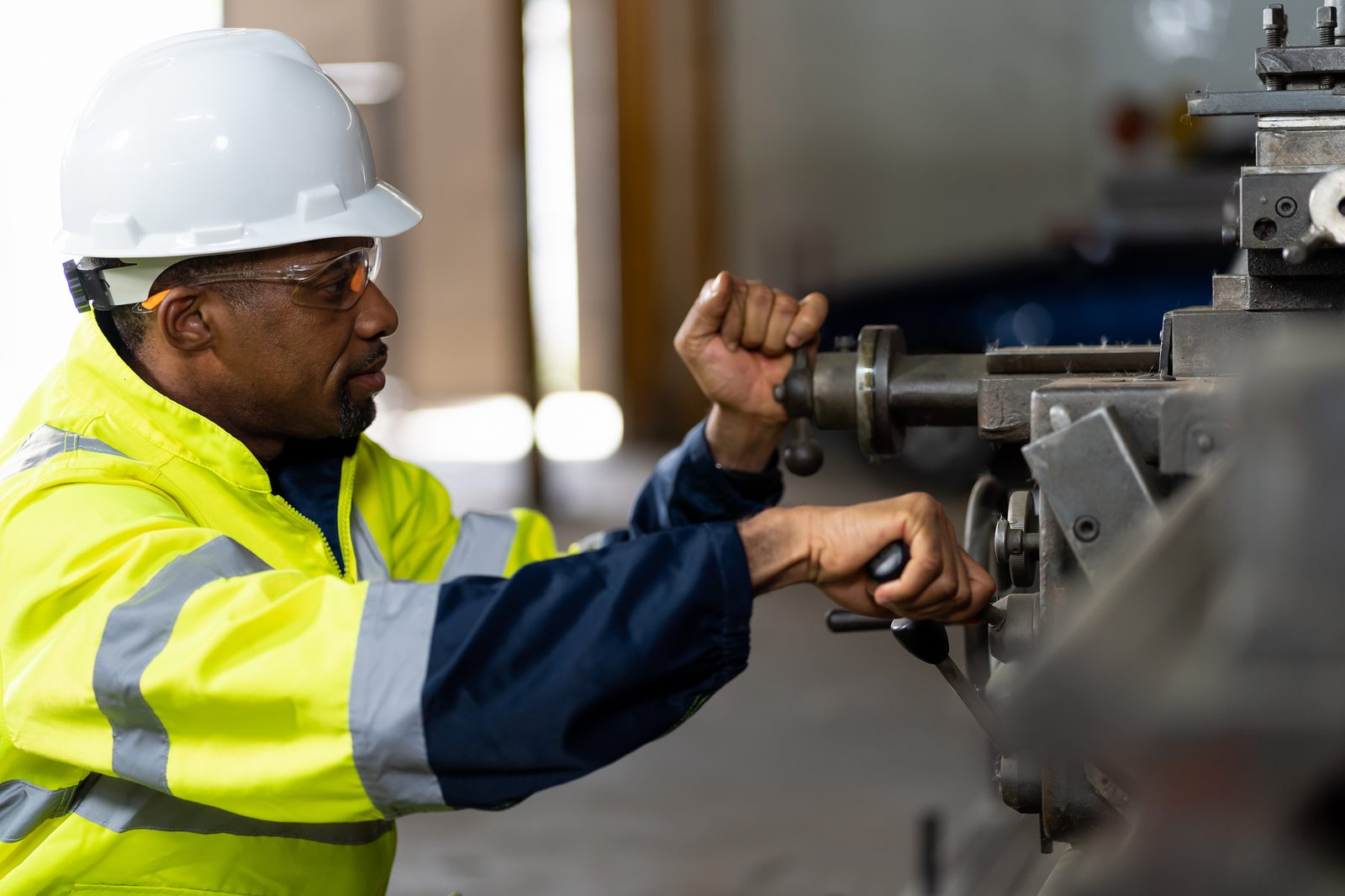 Machinist in a hard hat and safety vest setting up a machine on the shop floor