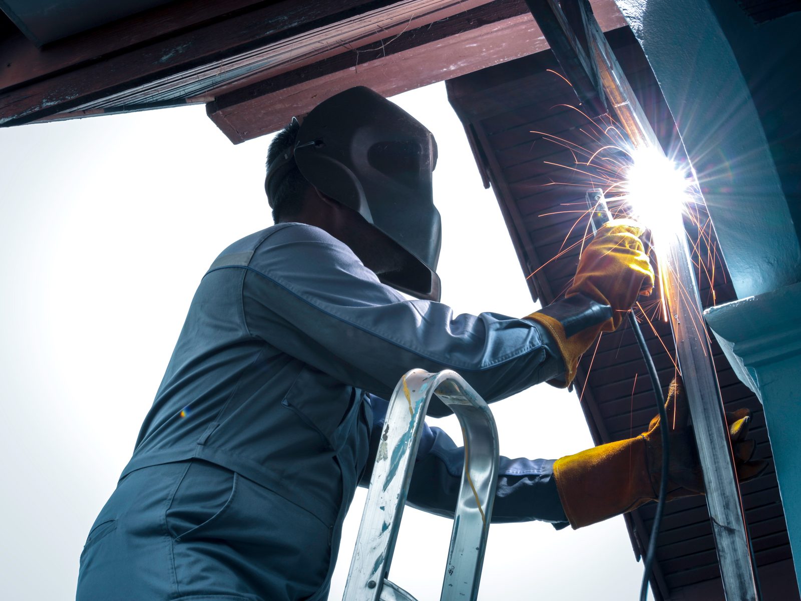 Welder in a protective helmet welding a steel beam, sparks flying